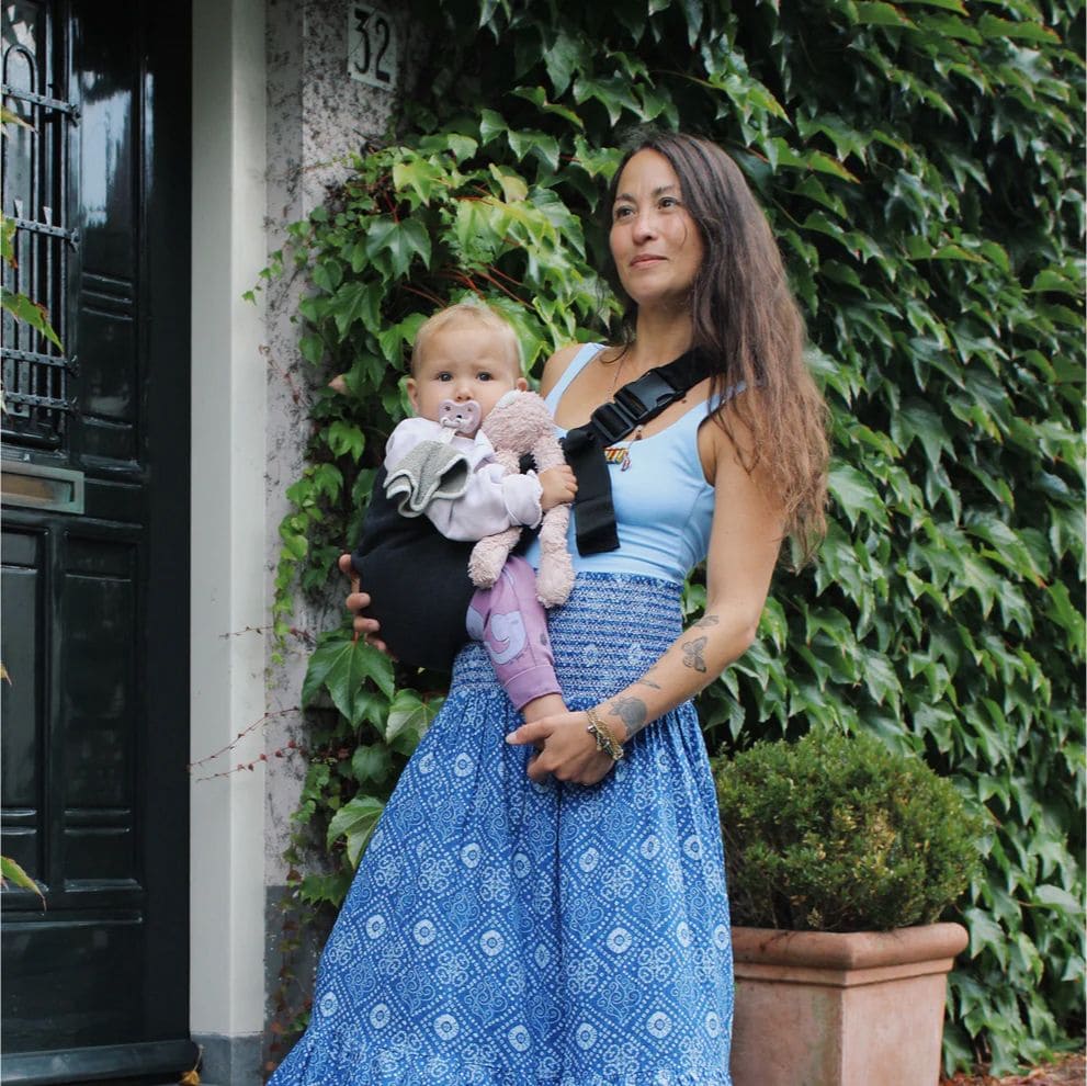 Madre elegante con vestido azul llevando a su bebé en el portabebés NAREVI, combinando estilo y comodidad